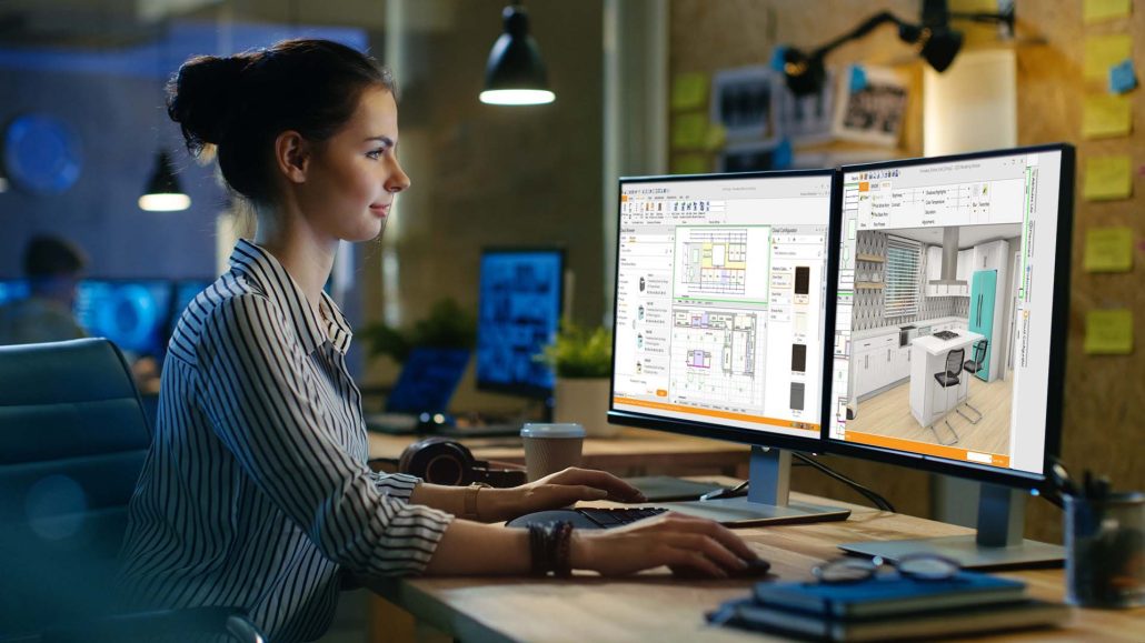 Woman working at two monitors showing 2020 Design kitchen floor plans and a 3D kitchen render