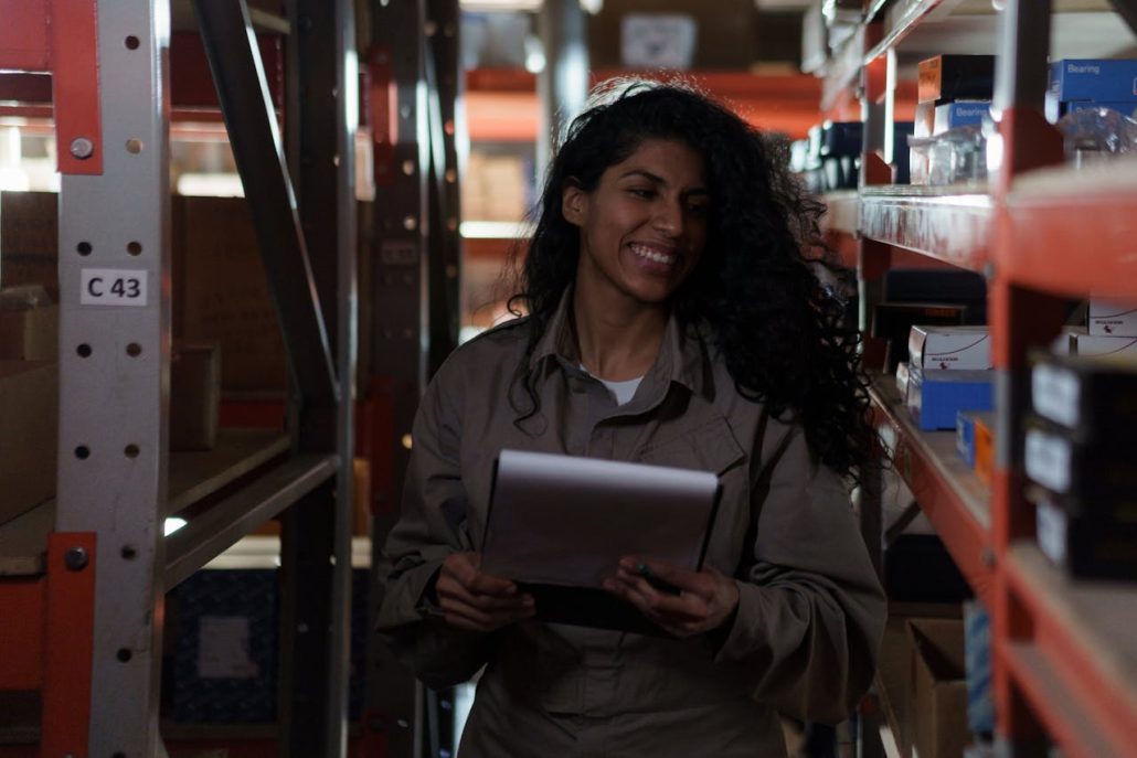 Smiling woman holding a tablet between warehouse shelves stocked with boxes