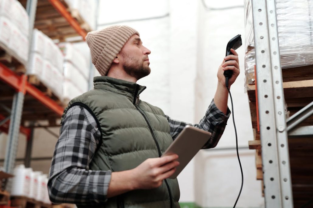 Warehouse worker scanning a pallet on a shelf with a handheld barcode scanner, tablet in the other hand